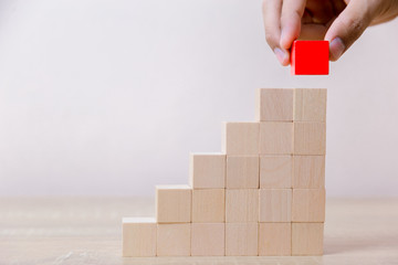Hand arranging red wood block stacking as step stair,With the concept of a thriving business going...