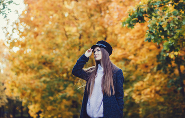 Young autumn woman in coat and black hat on leaves background