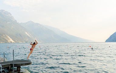 Young woman having fun and jumping into the water in lake lago di garda in Italy during holidays