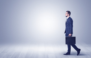 Fototapeta premium Successful businessman walking in front of an empty wall with briefcase on his hand 