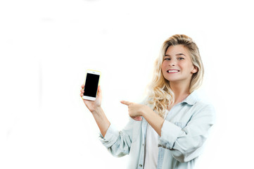 Fototapeta premium very beautiful young girl points to the smartphone, standing on a white isolated background.