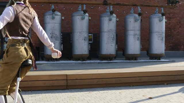 Young girl clown rides a unicycle and juggles balls outdoors
