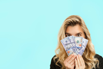 surprised emotional beautiful young girl holding money on a blue isolated background