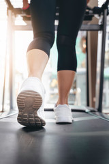 Fitness woman legs on running machine or treadmill in fitness gym with sunlight