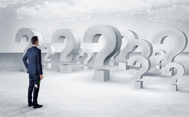 Businessman standing and looking to a bunch of question mark signs
