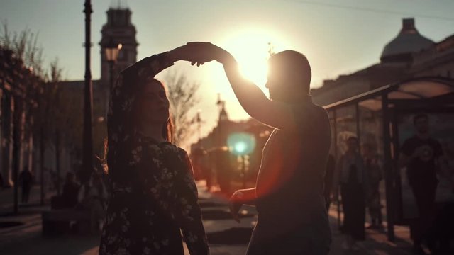 Young Couple Silhouettes Dancing On City Big Road And Sunset Sun In Background. Dark Shadows, No Recognizable Faces Of Lovers. Slow Motion.