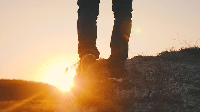 Hiker walking outdoors at sunset on the rock. Legs in trekking boots go along the mountain ridge against the backdrop of the sun Close up of leg walking in slow motion. Travel and adventure concept.