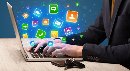 Businessman hand typing on laptop with flying application icons around

