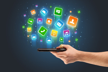 Businessman hand using phone with flying application icons around
