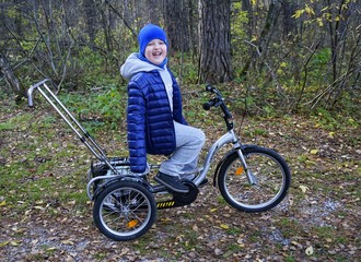 child autistic with disabilities on a tricycle with management for mom, in a blue cap and jacket in...