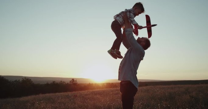 Middle of field at sunset , dad with his son , playing with a airplane and spending awesome time together.