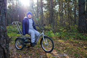 Fototapeta na wymiar child autistic with disabilities on a tricycle with management for mom, in a blue cap and jacket in the Park for a walk