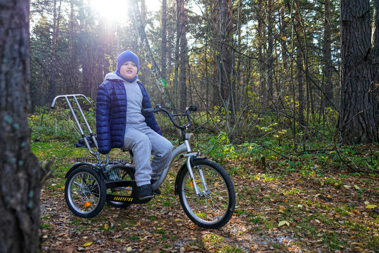 child autistic with disabilities on a tricycle with management for mom, in a blue cap and jacket in the Park for a walk