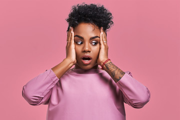 Fototapeta na wymiar Gorgeous beautiful female with dark skin, opens mouth wide and expresses surprisement, receives shocking news, isolated on yellow studio background with pink wall