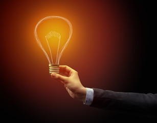 Hand holding light bulb on dark background. New idea concept