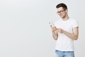 With songs through life. Portrait of happy and satisfied handsome european man installing cool music app on smartphone enjoying free trial period, holding gadget looking at screen wearing earphones