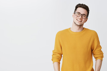 Waist-up shot of happy and delighted handsome young man in glasses and yellow sweater tilting head,...