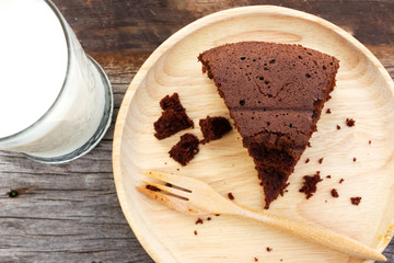 Closeup eaten chocalate cake on wooden plate with wood fork. Served with glass of milk. Food and drink background. Top view with copy space.