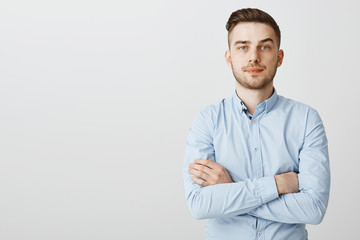 Smart ambitious and serious-looking young businessman in blue collar shirt holding hands crossed on...