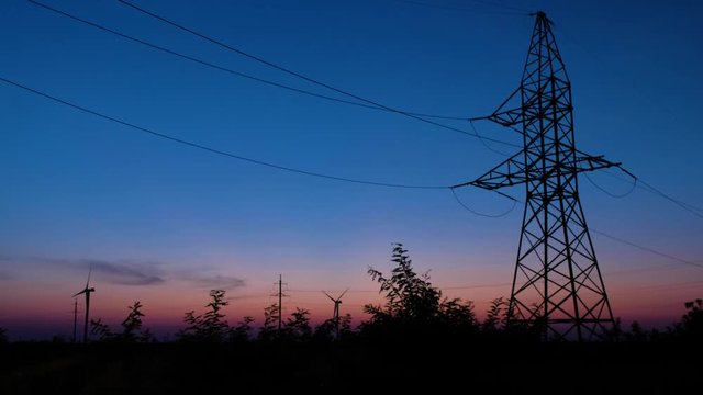 A silhouette of a power tower, standing against the last rays of setting sun