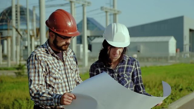 Two engineers discuss approve plan on big piece of paper. The plant is on the background. Slow motion