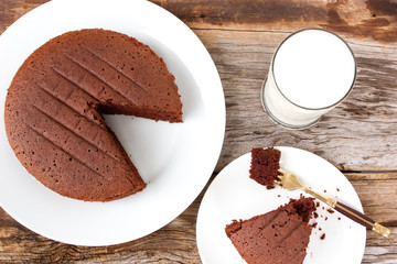 Homemade chocolate cake on white plate. Served with glass of milk. Top view. Food and drink background.