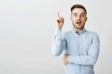 Guy got excellent idea sharing with team. Enthusiastic excited good-looking male in formal blue shirt raising index finger in eureka gesture holding breath and opening mouth while adding suggestion