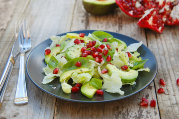 Vegetarian salad with avocado, greens, leaves, pomegranate and letuce leaves. Wooden rustic table.