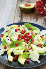 Vegetarian salad with avocado, greens, leaves, pomegranate and letuce leaves. Wooden rustic table.
