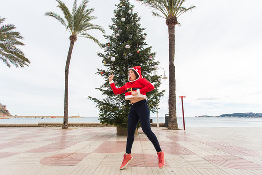 people, holidays and christmas concept - young funny and expressive woman dressed as santa claus jumping outdoors