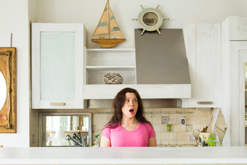 Housewives, emotions and people concept - Surprised young woman in the kitchen at home