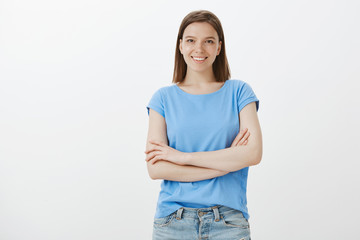 Studio shot of friendly confident european woman in blue t-shirt holding hands crossed on chest and...
