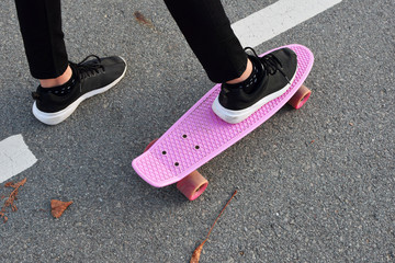 Teen girl feet in black sneakers riding on pink skateboard or penny board on gray asphalt...
