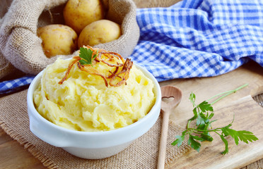 Mashed potatoes or Puree in white bowl with Crisp onion and parsley on wooden background.