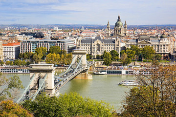 Chain Bridge or Szechenyi Bridge across Danube river in Budapest, Hungary, with old buildings and dome of St Stephen's Basilica or Szent Istvan Bazilika, in autumn.