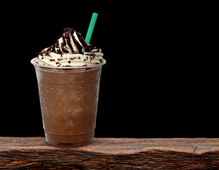 Frappuccino in takeaway cup on wooden table isolated on black background - obrazy, fototapety, plakaty