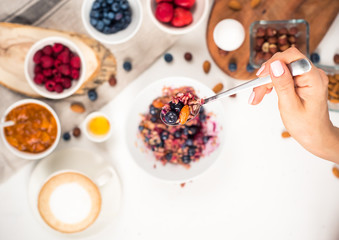 Top view showing hands eating porridge with honey nuts, blueberries on white wooden table selective focus, blurred background Good morning - healthy breakfast background