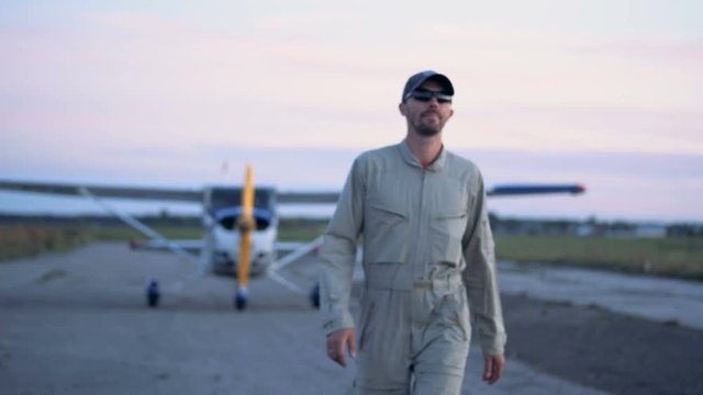 Male aviator is walking away from a biplane and stops with a smile