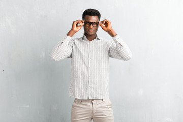 Young afro american man with glasses posing on textured grey wall