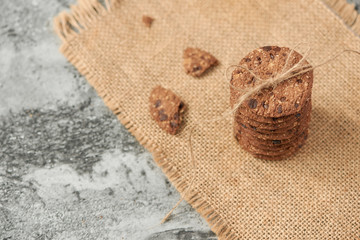 Stack of chocolate chip cookies tied with a rope and half with crumbs on burlap fabric on stone table