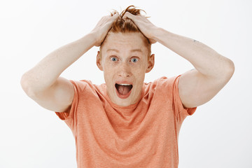 Attractive redhead sportsman with freckles being happy receiving offer to play in famous team, standing in orange t-shirt, touching hair and dropping jaw from amazement, gazing impressed and surprised