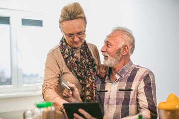 Senior couple using digital tablet and credit card in the kitchen at home for online shopping