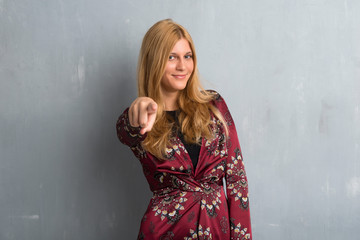 Blonde woman points finger at you with a confident expression on textured wall background