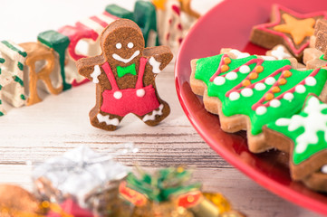 Tasty and cute baked Christmas cookies (gingerbread) with beautiful xmas decoration in red plate on light wooden table background, close up, copy space (text space)