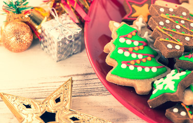 Tasty and cute baked Christmas cookies (gingerbread) with beautiful xmas decoration in red plate on light wooden table background, close up, copy space (text space)