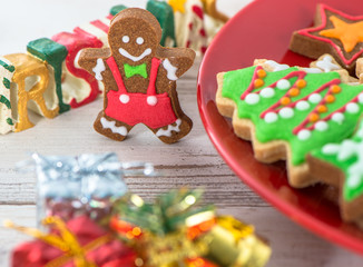 Tasty and cute baked Christmas cookies (gingerbread) with beautiful xmas decoration in red plate on light wooden table background, close up, copy space (text space)