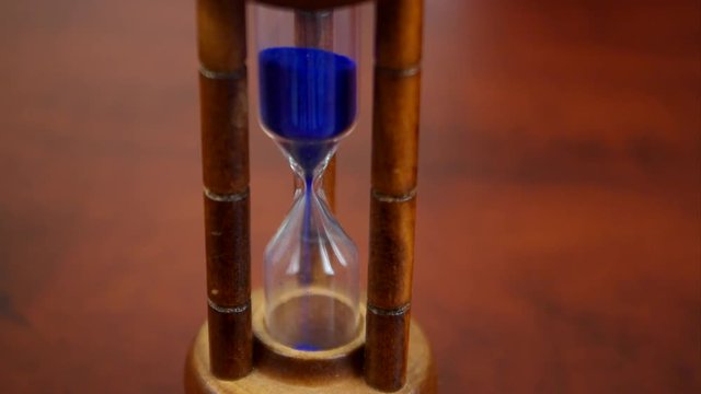 Running time theme with old hourglass close up on brown wooden table