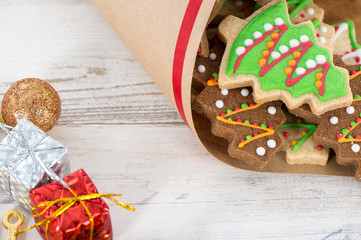 Tasty and cute baked Christmas cookies (gingerbread) with beautiful xmas decoration in paper bag on light wooden table background, close up, copy space (text space)