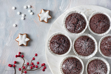 Flat lay with red berry decoration on white rustic background and chocolate muffins in white paper cups with sugar icing on white