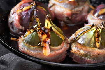 Closeup on baked fig wrapped in bacon, stuffed with pine nuts and served with honey
